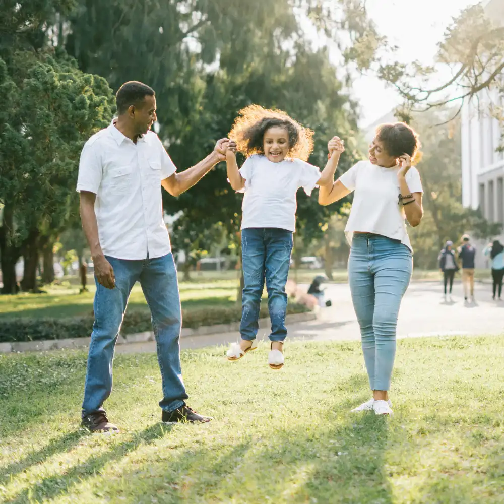 Happy family playing outdoors as parents lift their smiling child in a sunny park.