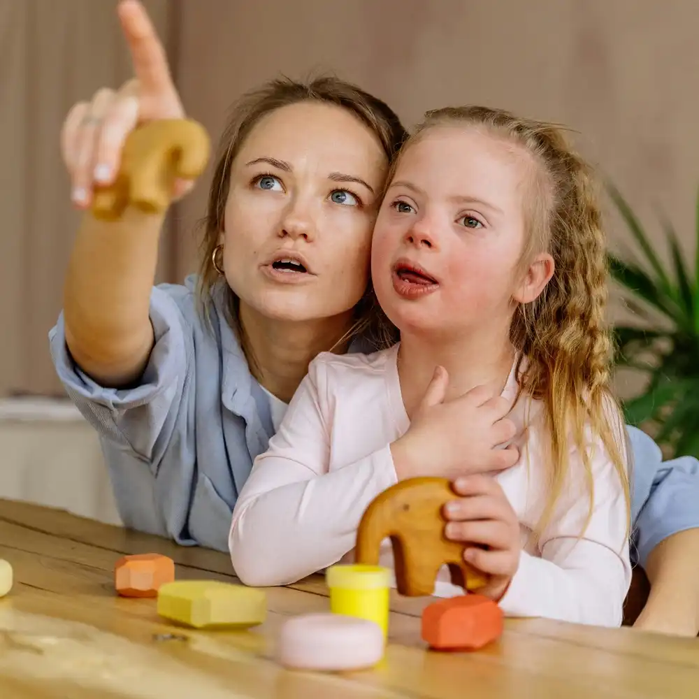 Teacher supporting a young girl with Down syndrome during a learning activity using educational wooden toys.