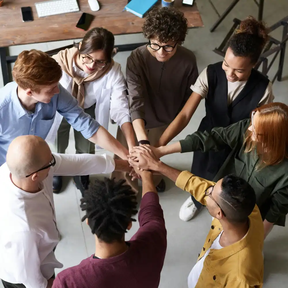 Diverse team standing in a circle and joining hands together to show unity, teamwork, and collaboration in a modern office setting