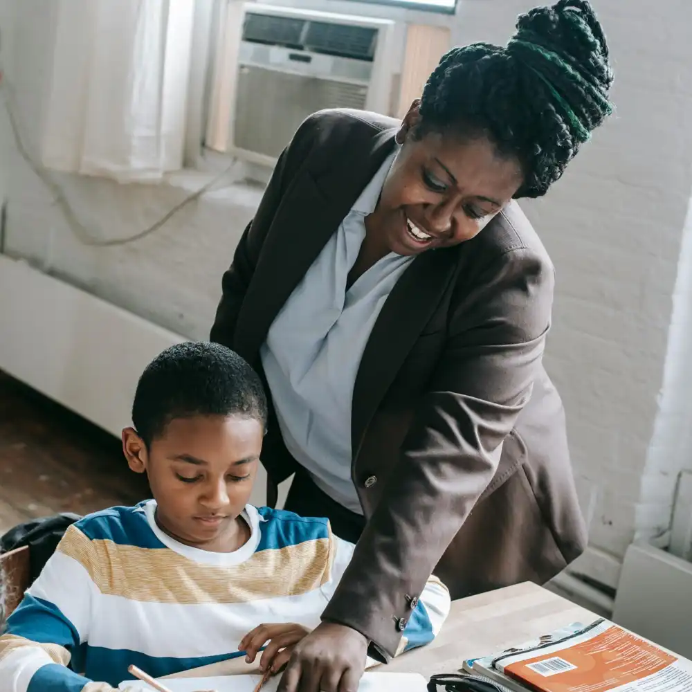 Tutor helping a young student with homework and learning support at a classroom desk